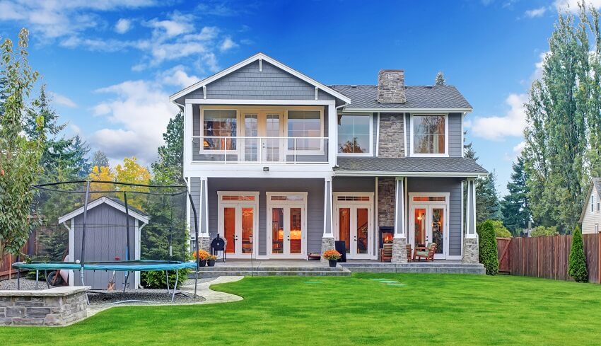 Grey house with stone chimney, back porch and trampoline on ground