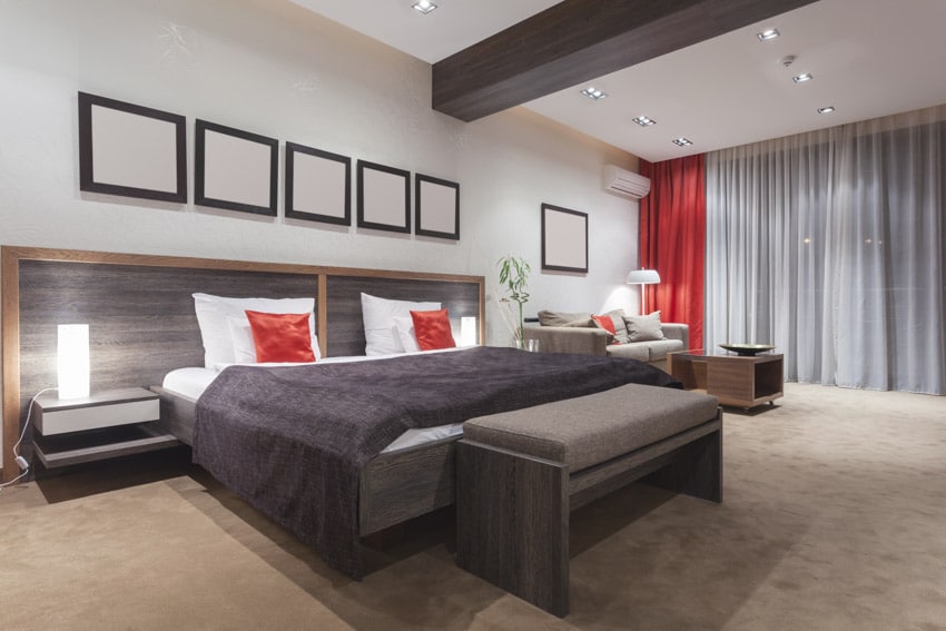 Bedroom with bedding, pillows, headboard, nightstands, bench, lamps, and window curtains