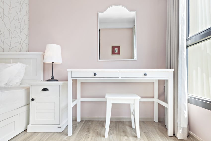 Bedroom with vanity table, small stool, nightstand, lamp, curtains, mirror, and wood flooring
