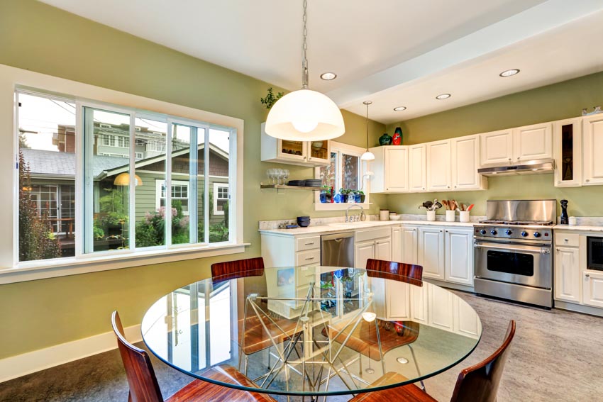 Sage kitchen and dining area with glass table, chairs, white cabinets, oven, stove, and windows