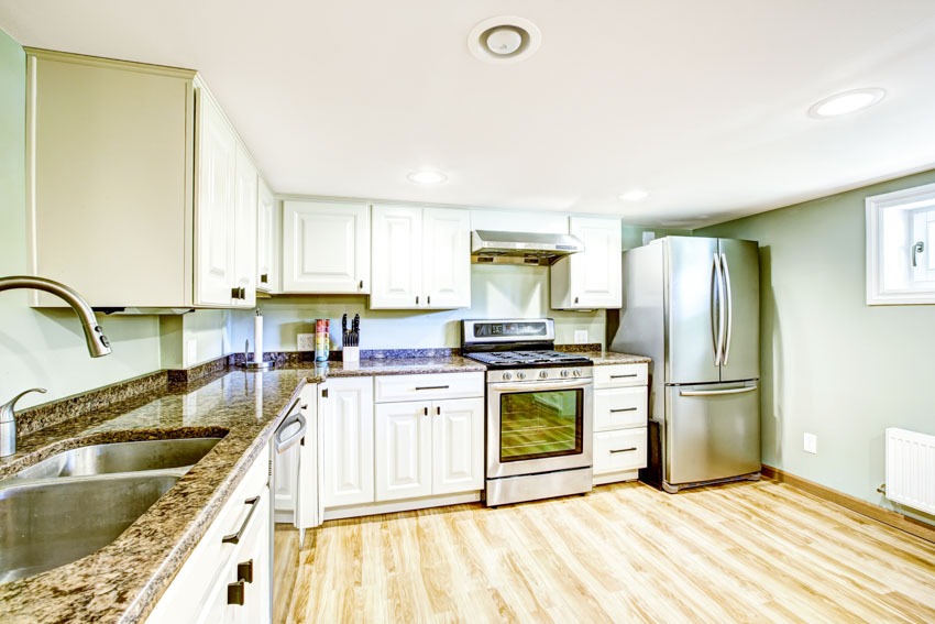 Kitchen with wood planked floor, white cabinetry, wall in sage, countertop, sink, refrigerator, oven, and stove