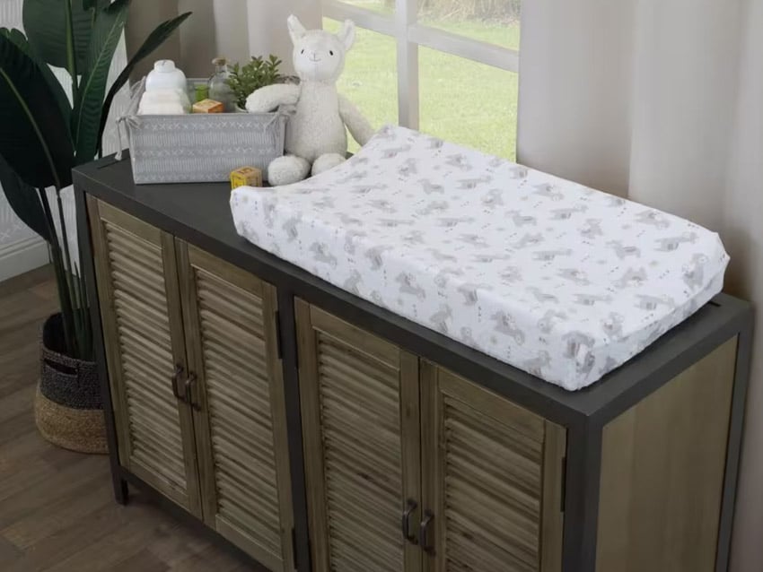Nursery with wooden long dresser, changing pad, wood floor, window, and indoor plant